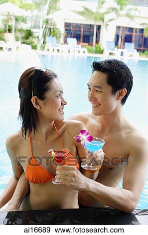 Couple in swimming pool holding cocktail drinks, smiling at each other View Large Photo Image Stock Photo - Couple in swimming pool holding cocktail drinks, smiling at each other. Fotosearch