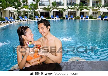 Stock Photo - Couple in swimming pool, toasting with cocktails . Fotosearch