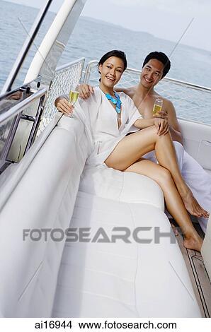 Couple lounging on yacht, holding champagne glasses View Large Photo Image Picture - Couple lounging on yacht, holding champagne glasses . Fotosearch