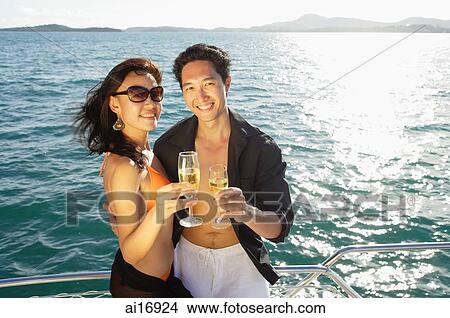Picture - Couple on boat deck, standing next to railing, holding champagne glasses, smiling at camera . Fotosearch