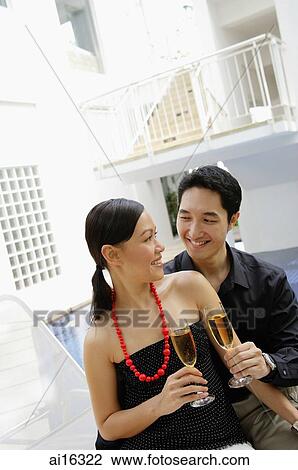 Couple sitting by poolside, looking at each other, holding champagne glasses View Large Photo Image Stock Image - Couple sitting by poolside, looking at each other, holding champagne glasses . Fotosearch