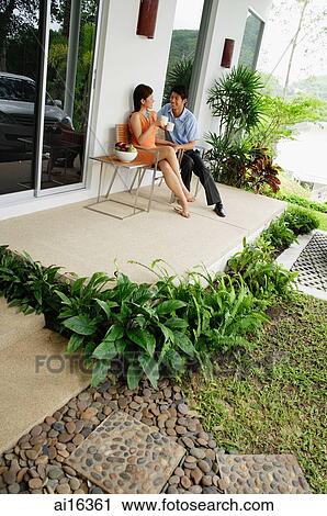 Stock Image - Couple sitting on patio having coffee . Fotosearch