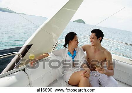 Couple sitting on stern of yacht, holding champagne glasses View Large Photo Image Stock Image - Couple sitting on stern of yacht, holding champagne glasses . Fotosearch