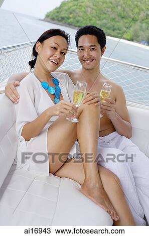 Couple sitting on yacht, holding champagne glasses, smiling at camera View Large Photo Image Stock Image - Couple sitting on yacht, holding champagne glasses, smiling at camera . Fotosearch