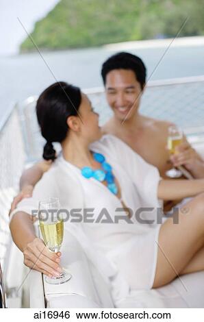 Couple sitting on yacht holding champagne glasses View Large Photo Image Stock Photograph - Couple sitting on yacht holding champagne glasses . Fotosearch