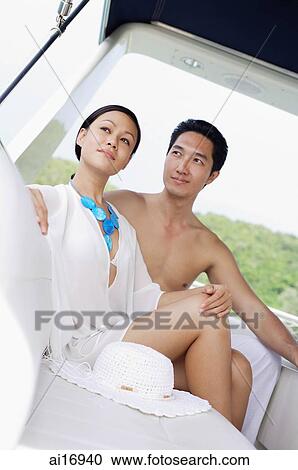 Stock Image - Couple sitting on yacht, man looking at woman, woman looking away. Fotosearch