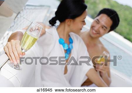 Couple sitting side by side on yacht holding champagne glasses View Large Photo Image Stock Photography - Couple sitting side by side on yacht holding champagne glasses . Fotosearch