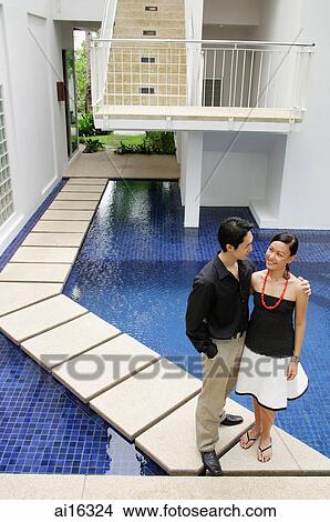 Couple standing by swimming pool, man with hand on womans shoulder View Large Photo Image Picture - Couple standing by swimming pool, man with hand on womans shoulder . Fotosearch