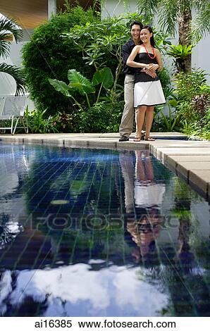Couple standing by swimming pool, man embracing woman, both smiling at camera View Large Photo Image Stock Photography - Couple standing by swimming pool, man embracing woman, both smiling at camera. Fotosearch