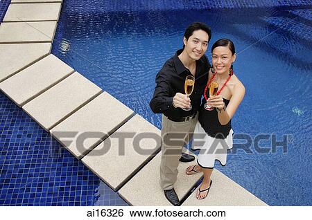 Couple standing by swimming pool, looking up at camera, holding champagne glasses View Large Photo Image Stock Photograph - Couple standing by swimming pool, looking up at camera, holding champagne glasses . Fotosearch