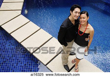 Couple standing by swimming pool, looking up at camera View Large Photo Image Stock Photography - Couple standing by swimming pool, looking up at camera . Fotosearch