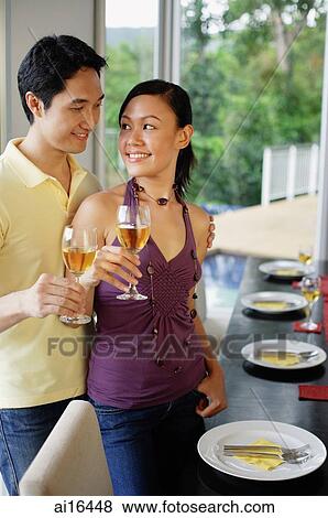 Couple standing next to dining table, holding wine glasses, looking at each other View Large Photo Image Stock Photo - Couple standing next to dining table, holding wine glasses, looking at each other. Fotosearch
