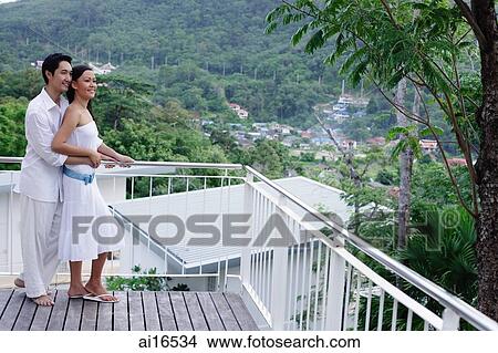Couple standing on balcony, man embracing woman from behind View Large Photo Image Picture - Couple standing on balcony, man embracing woman from behind . Fotosearch