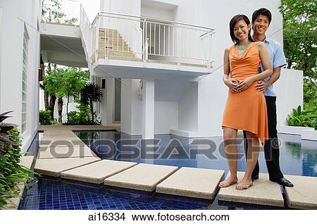 Couple standing outside house, next to swimming pool, looking at camera View Large Photo Image Picture - Couple standing outside house, next to swimming pool, looking at camera . Fotosearch