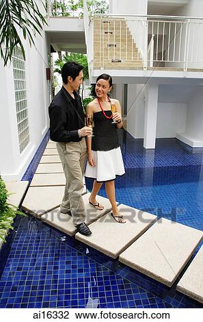 Couple walking by swimming pool, champagne glasses in hand View Large Photo Image Stock Image - Couple walking by swimming pool, champagne glasses in hand . Fotosearch