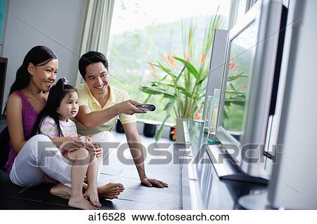 Stock Photo - Family of three in front of TV, man pointing remote control at TV . Fotosearch