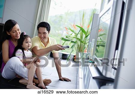 Family of three watching TV, father holding remote control View Large Photo Image Stock Photo - Family of three watching TV, father holding remote control. Fotosearch