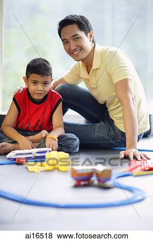 Father and son looking at camera, toy train set on floor in front of them View Large Photo Image Stock Photo - Father and son looking at camera, toy train set on floor in front of them . Fotosearch