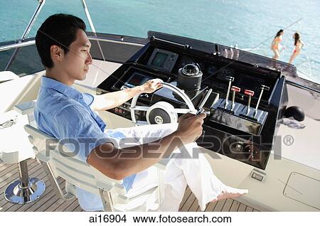 Picture - Man at helm of yacht, people in the background . Fotosearch
