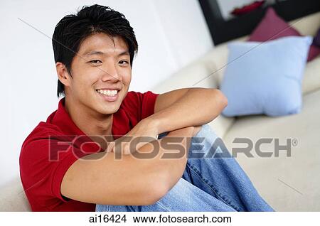 Man sitting on sofa, arms crossed, hugging knees, looking at camera View Large Photo Image Picture - Man sitting on sofa, arms crossed, hugging knees, looking at camera. Fotosearch