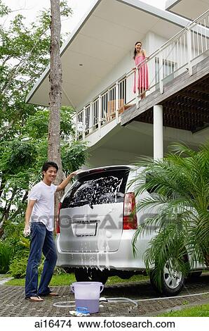 Picture - Man washing car, woman standing on balcony looking down . Fotosearch