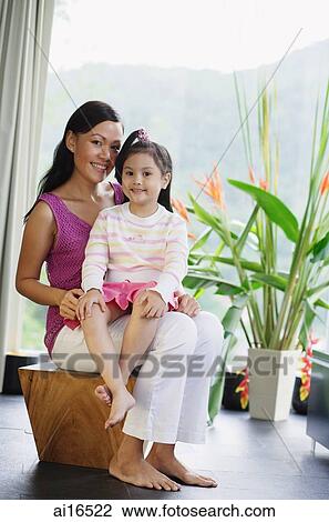 Stock Image - Mother with young girl on her lap, smiling at camera . Fotosearch