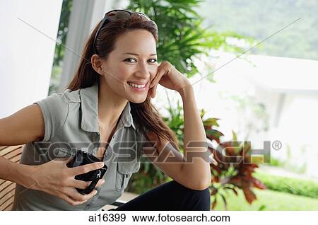 Stock Photo - Woman holding coffee mug, hand on chin, smiling. Fotosearch
