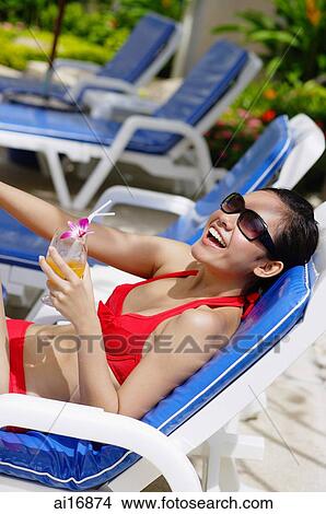 Woman in bikini, sitting on deck chair, holding drink, smiling View Large Photo Image Picture - Woman in bikini, sitting on deck chair, holding drink, smiling . Fotosearch