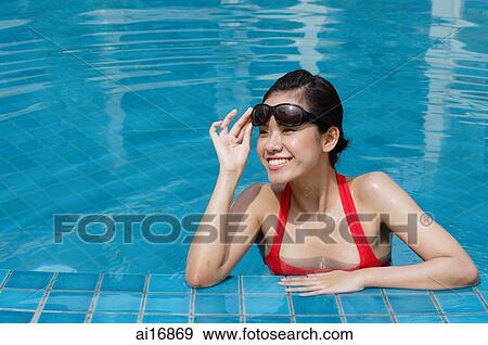 Woman leaning on edge of swimming pool, adjusting sunglasses, smiling View Large Photo Image Stock Photo - Woman leaning on edge of swimming pool, adjusting sunglasses, smiling . Fotosearch