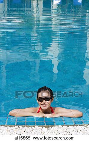Woman leaning on edge of swimming pool, wearing sunglasses, smiling View Large Photo Image Stock Photography - Woman leaning on edge of swimming pool, wearing sunglasses, smiling . Fotosearch