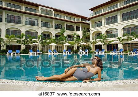 Woman lying next to swimming pool, building in the background View Large Photo Image Stock Photo - Woman lying next to swimming pool, building in the background . Fotosearch
