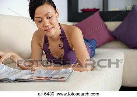 Woman lying on sofa, reading a magazine View Large Photo Image Stock Image - Woman lying on sofa, reading a magazine. Fotosearch