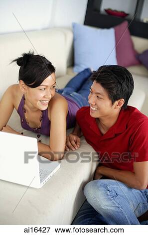 Woman lying on sofa with laptop, man sitting on floor next to her View Large Photo Image Stock Photo - Woman lying on sofa with laptop, man sitting on floor next to her. Fotosearch