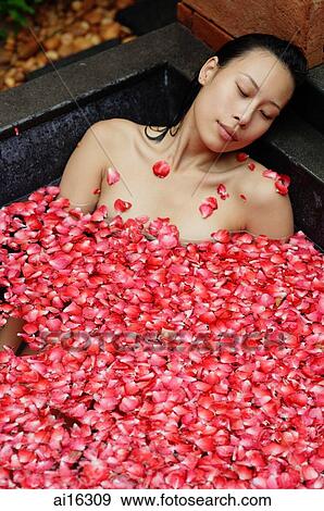 Stock Photo - Woman relaxing in tub with floating rose petals, eyes closed . Fotosearch