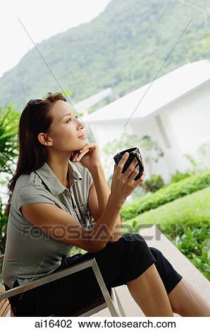 Woman sitting, holding coffee mug, hand on chin View Large Photo Image Stock Image - Woman sitting, holding coffee mug, hand on chin. Fotosearch