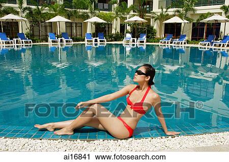 Woman sitting next to swimming pool, wearing bikini View Large Photo Image Stock Image - Woman sitting next to swimming pool, wearing bikini. Fotosearch