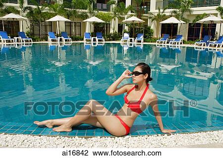 Woman sitting next to swimming pool, adjusting sunglasses View Large Photo Image Stock Image - Woman sitting next to swimming pool, adjusting sunglasses. Fotosearch