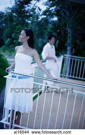 Woman standing on balcony looking away, man leaning on railing in the background View Large Photo Image Picture - Woman standing on balcony looking away, man leaning on railing in the background . Fotosearch