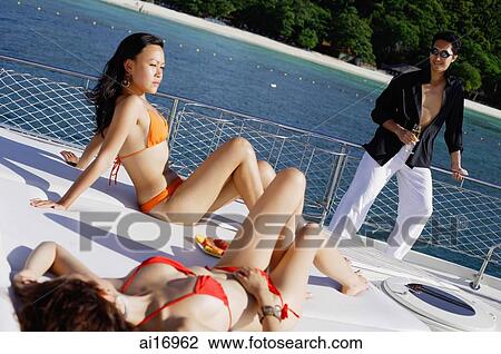 Women sitting on boat deck, man standing next to railing, holding champagne glass View Large Photo Image Stock Image - Women sitting on boat deck, man standing next to railing, holding champagne glass . Fotosearch