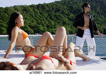 Women sunbathing on boat deck, man standing next to railing View Large Photo Image Stock Image - Women sunbathing on boat deck, man standing next to railing. Fotosearch