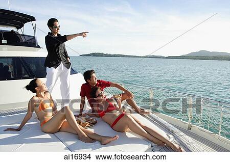 Young adults on boat deck, man standing and pointing to the distance View Large Photo Image Picture - Young adults on boat deck, man standing and pointing to the distance . Fotosearch