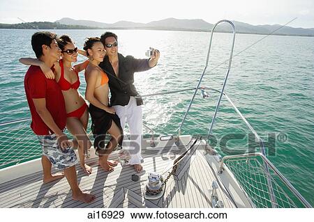 Stock Photo - Young adults on boat deck, taking a picture . Fotosearch