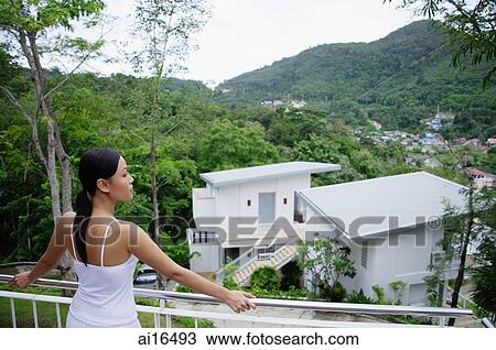 Stock Image - Young woman leaning on railing, looking out at view . Fotosearch