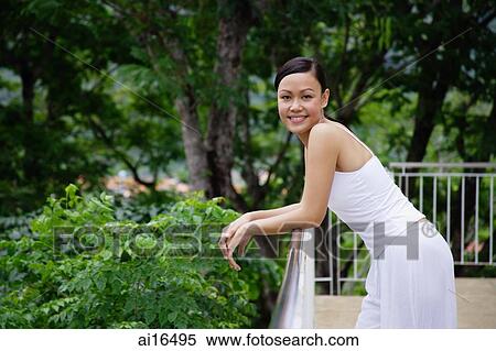 Stock Photography - Young woman leaning on railing, looking at camera . Fotosearch