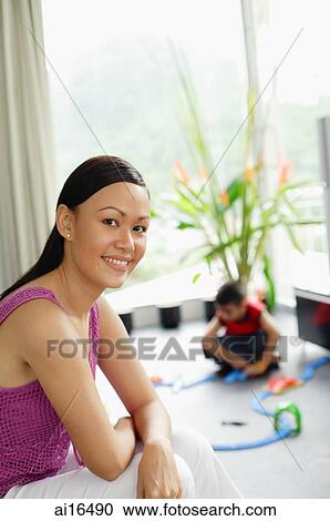 Stock Image - Young woman looking at camera, child in the background . Fotosearch