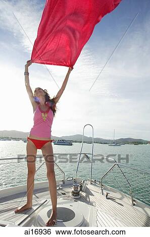Stock Photograph - Young woman on windy boat deck, holding piece of cloth in the air . Fotosearch