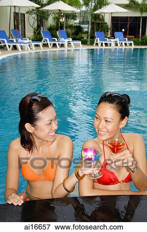 Young women in swimming pool, smiling at each other, holding cocktails View Large Photo Image Stock Photo - Young women in swimming pool, smiling at each other, holding cocktails . Fotosearch