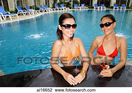 Stock Image - Young women in swimming pool, wearing sunglasses, smiling at camera . Fotosearch