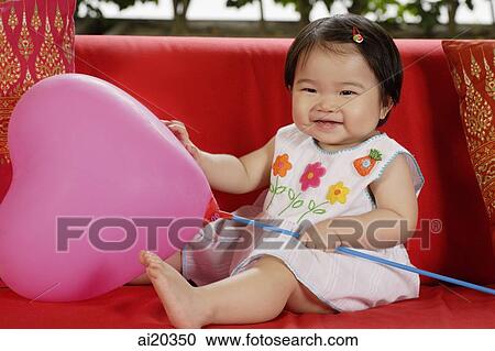 Baby girl sitting on a red sofa with pink balloon View Large Photo Image Stock Image - Baby girl sitting on a red sofa with pink balloon. Fotosearch