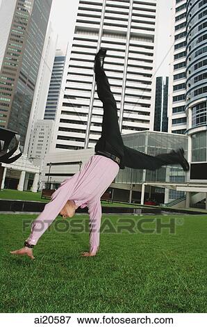 Businessman doing cartwheels on grass, buildings in the background View Large Photo Image Stock Photo - Businessman doing cartwheels on grass, buildings in the background. Fotosearch